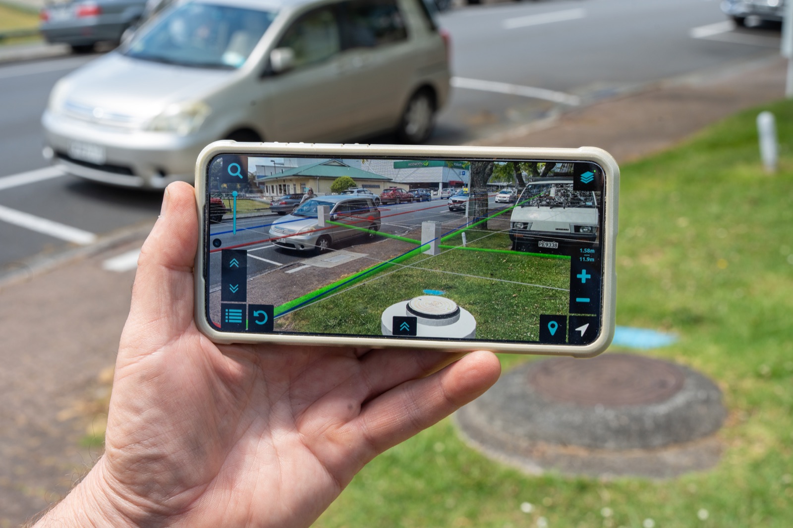 Hand holding a landscape phone showing mapped utility lines over a street and grass verge in Augview.