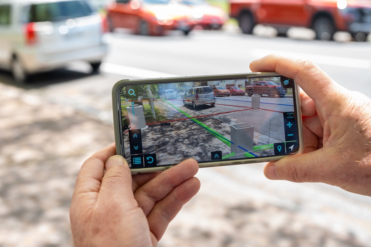 Two hands holding a landscape phone, with a thumb on the Augview mapped-services display.